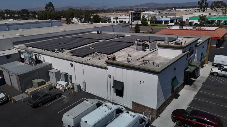 Aerial drone view of commercial building with solar array, parking lot and service vans